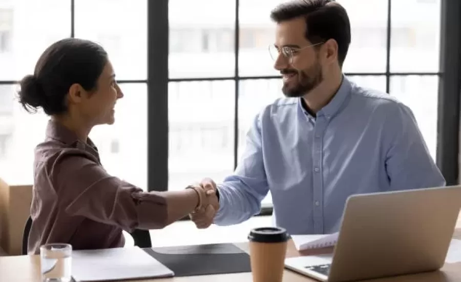 Confident smiling male hr manager employer in eyewear shaking hands with happy indian ethnicity female job seeker after successful interview. Diverse young business people making agreement in office.